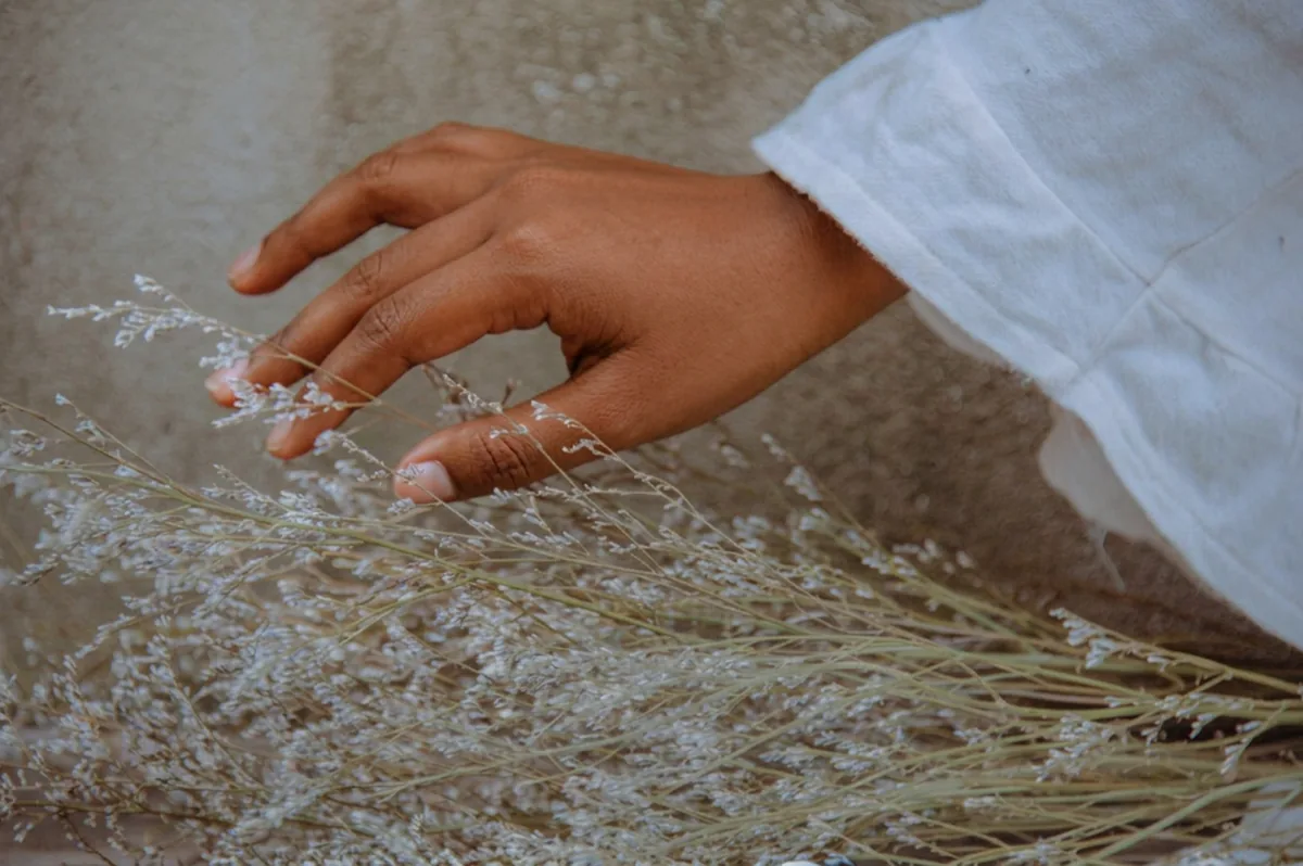 A hand brushing through dried wildflowers beside a white linen sleeve
